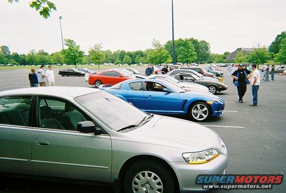 Several cars parked in a lot, with people standing around them