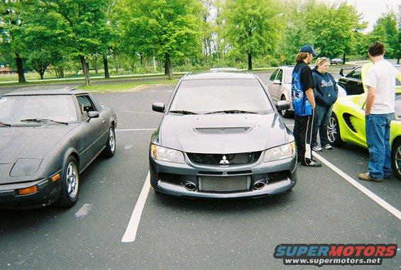 Dark grey Mitsubishi Lancer Evolution IX with a hood scoop and large front grille parked in a lot