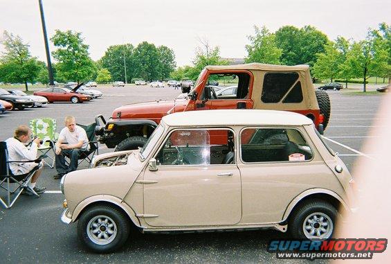 Tan classic Mini Cooper parked next to a red Jeep Wrangler, two men sitting in chairs nearby