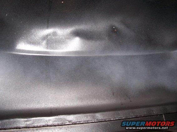Close-up of a dented, dark-colored metal panel with a horizontal crease