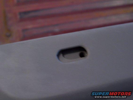 Close-up of a gray car door panel with a small oval cutout and a screw hole