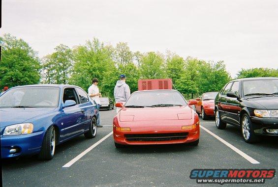 Red sports car with pop-up headlights and a wide front grille, parked in a lot