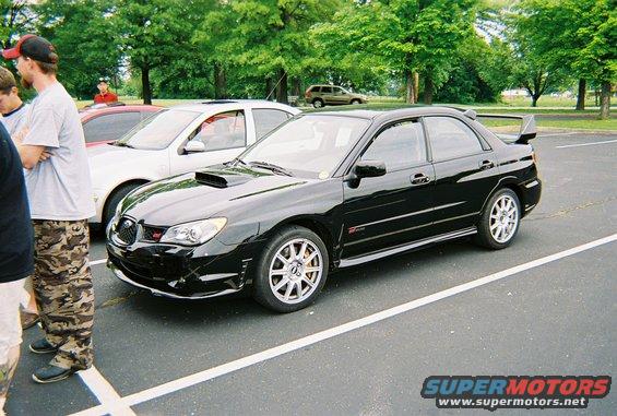 Black sedan with a rear spoiler and hood scoop, parked in a lot