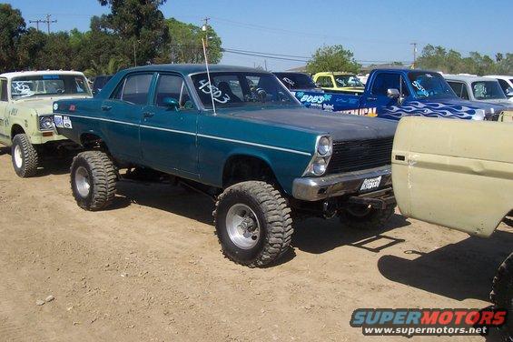 Teal sedan with lifted suspension and large tires, parked next to other vehicles