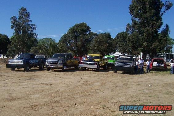 Several pickup trucks parked in a dirt lot under a clear blue sky
