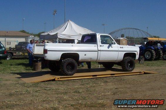 White pickup truck on a scale, side view. It has large tires and a lifted suspension