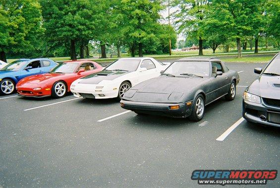 Dark gray Mazda RX-7 parked in a lot with other cars. It has pop-up headlights