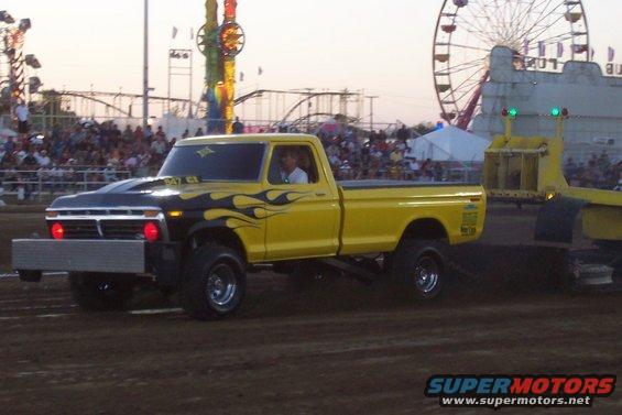 Yellow pickup truck with black flame decals and a lifted suspension, pulling a trailer at a fairground