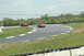 1993 Ford Mustang - A red 1993 Ford Mustang navigates a turn on a sunny day at the racetrack, with other vehicles visible in the background.