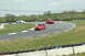 1993 Ford Mustang - Three cars are racing on a paved track with grassy shoulders and tire barriers.