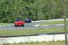 1993 Ford Mustang - Two vehicles navigate a turn on a paved racetrack surrounded by trees.