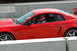 1993 Ford Mustang - A red coupe with a racing driver is seen from the side on a track. The vehicle's body style suggests it is a 2000 Ford Mustang.