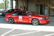 1993 Ford Mustang - A red 1993 Ford Mustang Cobra race car, number 99, is parked under a covered area with other vehicles present.