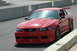 1993 Ford Mustang - A red Ford Mustang with a large rear spoiler is parked on the side of a race track.