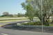 1993 Ford Mustang - A distant white car drives on a race track surrounded by trees and concrete barriers on a clear day.