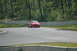 1993 Ford Mustang - Red Ford Mustang driving on a race track with trees and concrete barriers in the background.