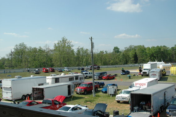 Race track parking area with trailers, trucks, cars, and RVs under a blue sky
