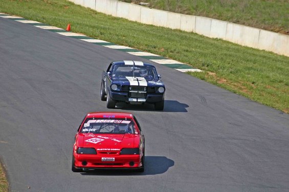 Red 1993 Ford Mustang Cobra race car in foreground, blue Mustang race car behind it on track