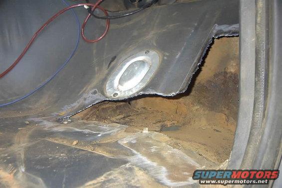 Interior floor of a vehicle with significant rust and damage, showing cut metal and exposed undercarriage