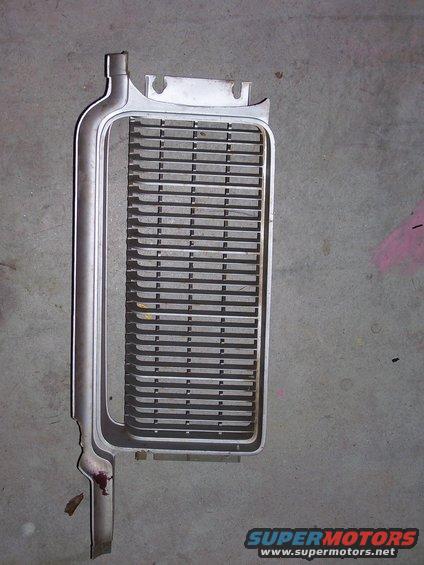 Car grille with horizontal slats, silver colored, lying on a concrete floor