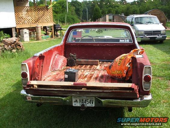 Red pickup truck bed with a battery and a large orange bag. A silver van is parked behind it