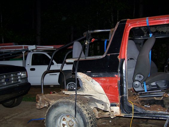 partially disassembled off-road vehicle with roll cage, white pickup truck behind it