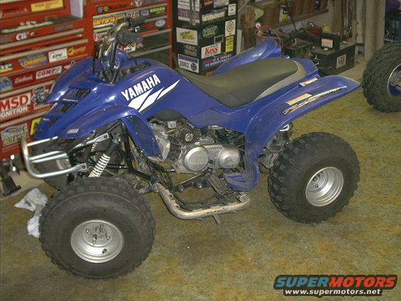 Blue Yamaha ATV parked in a garage with tool chests in the background. A sticker on a tool chest says '2002'