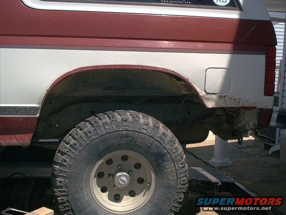 Rear wheel well and quarter panel of a two-tone red and white SUV, possibly a Ford Bronco