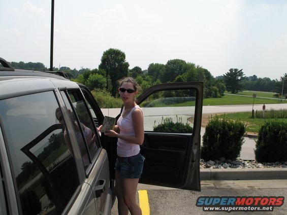 Woman holding a book stands next to an open SUV door