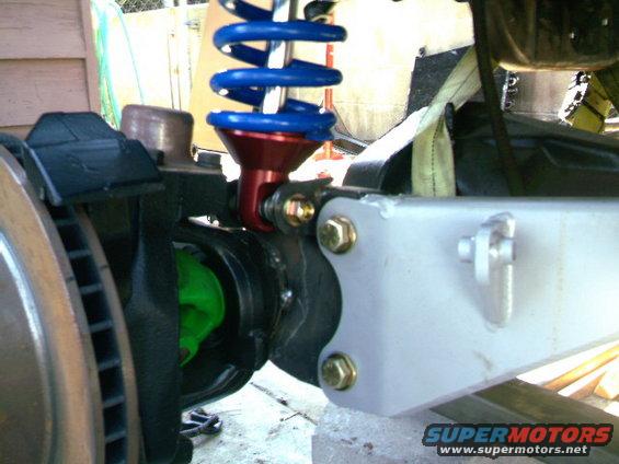 Close-up of a suspension component with a blue coilover shock and red bracket. Text at bottom reads SUPERMOTORS