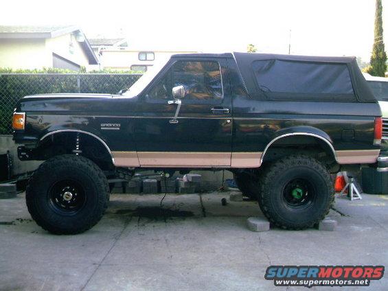 Side view of a black lifted 1989 Ford Bronco with tan trim and a soft top