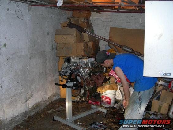 Engine on stand in cluttered basement with a person inspecting it