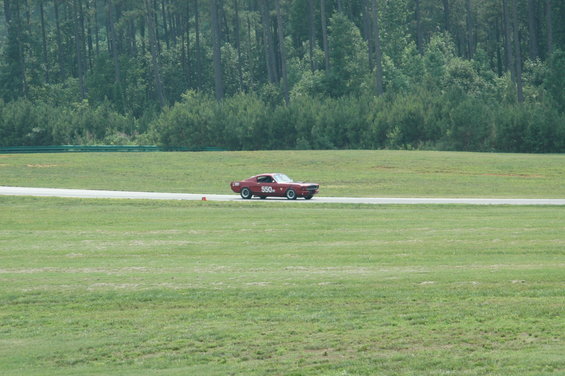 Red 1969 Ford Mustang on a race track with trees in the background. The car has the number 550 on its door