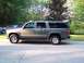 2002 Chevrolet Suburban - A gray Chevrolet Suburban is parked on the side of a road with trees and a house in the background.