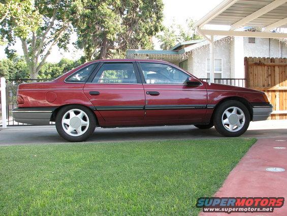 Maroon sedan parked on grass next to driveway under a carport