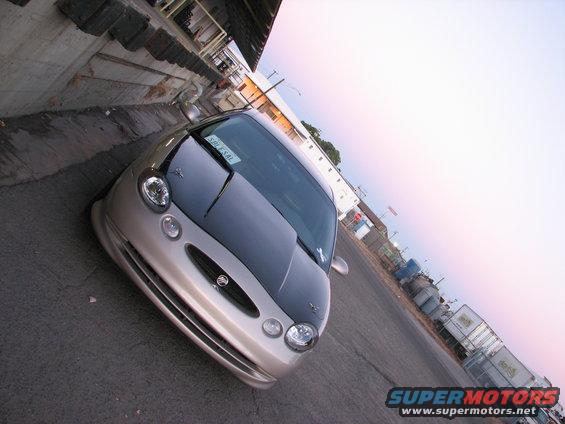Front of a silver Mercury Cougar with a dark hood parked next to a concrete loading dock