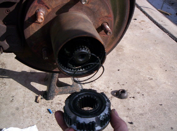 Hand holding a manual locking hub assembly next to a vehicle's wheel hub and brake rotor