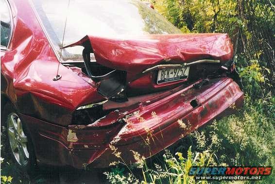 red sedan with heavily damaged rear bumper and trunk, parked in tall grass