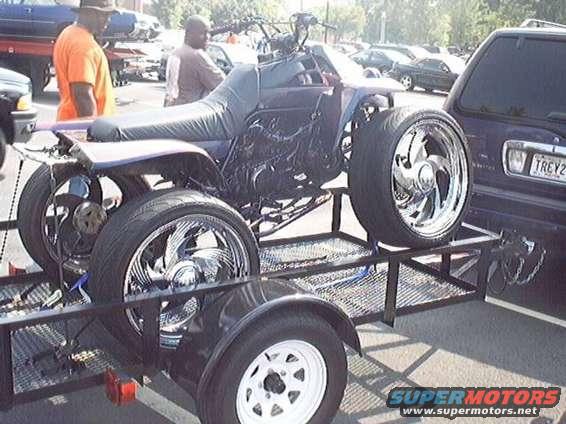 Custom ATV with large chrome wheels on a trailer next to a dark SUV