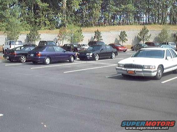 Cars parked in lot, including a white sedan in foreground and purple sedan behind it