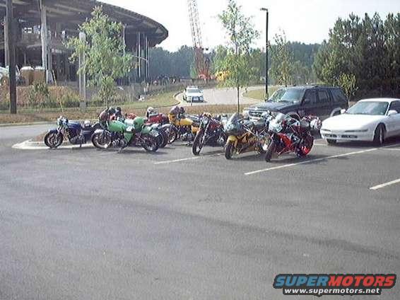 Several motorcycles and a white car parked in a lot