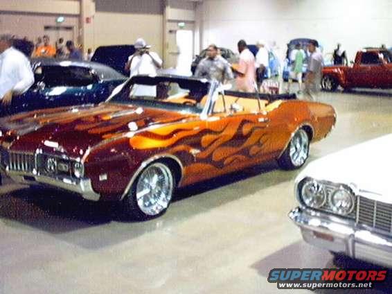 Orange convertible with flame graphics, chrome wheels, and a white interior, viewed from the front three-quarter angle
