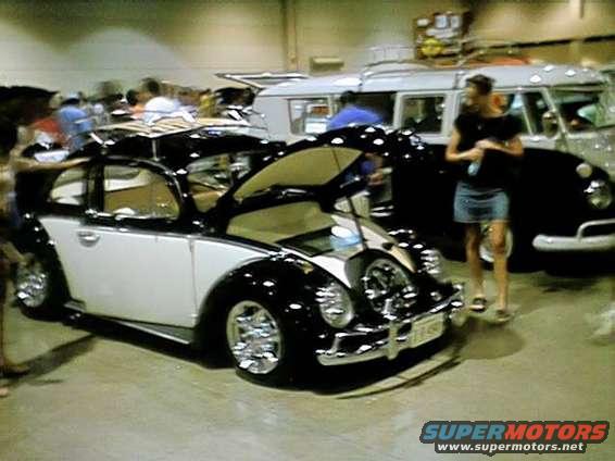 Black and white Volkswagen Beetle with hood open, chrome wheels, and a roof rack