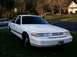 1996 Ford Crown Victoria - A white sedan is parked on a grassy area in front of a house with trees in the background.