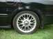 2000 Ford Taurus - A black sedan's rear wheel and side panel are visible, with grass in the background and a watermark at the bottom right.