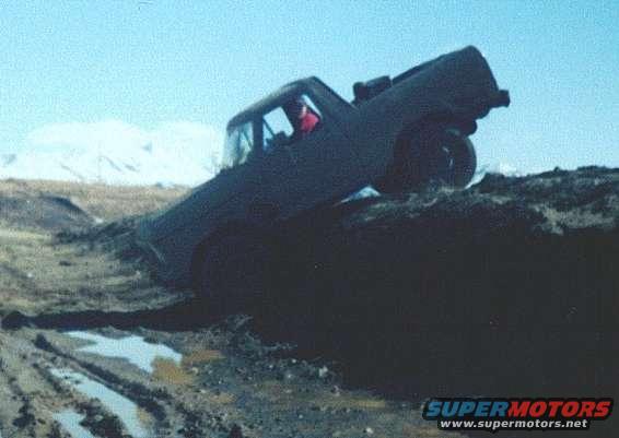 Truck tilted on its side, stuck in a muddy ditch with snow-capped mountains in the background