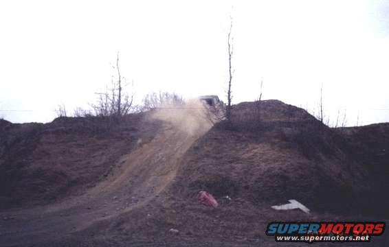White SUV cresting a dirt hill, kicking up dust