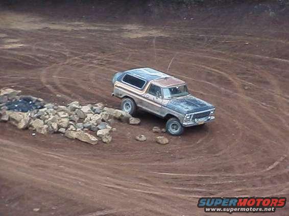 1978 Ford Bronco driving on a dirt track with rocks