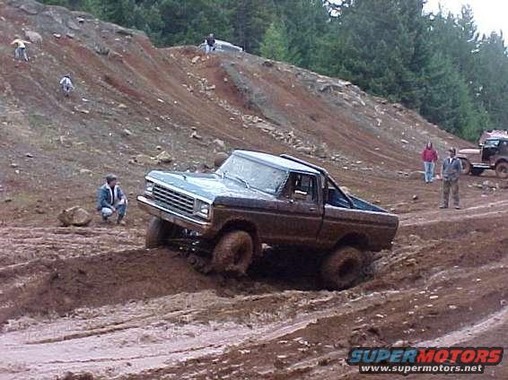 Muddy 1979 Ford F-Series pickup truck navigating a dirt track with other vehicles and people on a hillside