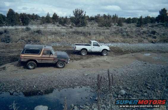 1978 Ford Bronco parked next to a white pickup truck on a dirt road
